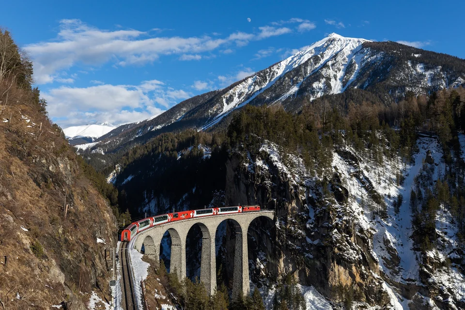 Red Glacier Express train crossing the curved stone Landwasser Viaduct below snowy peaks in Switzerland