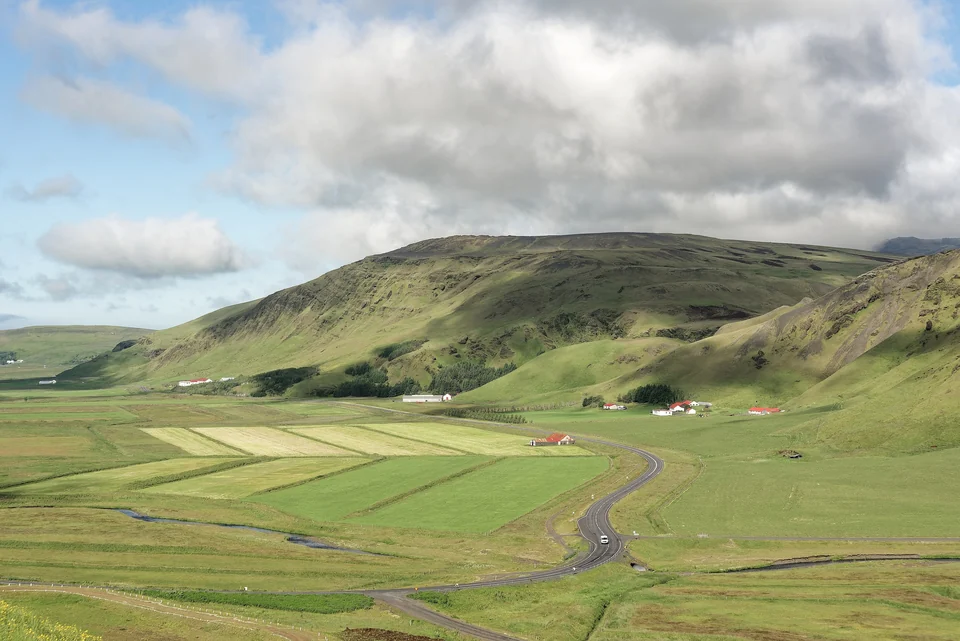 Route 1 winding through green farmland and hills in southern Iceland under a cloudy sky