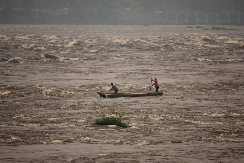 Two fishermen in a wooden canoe working the fast brown rapids of the Congo River near Kinshasa and Brazzaville