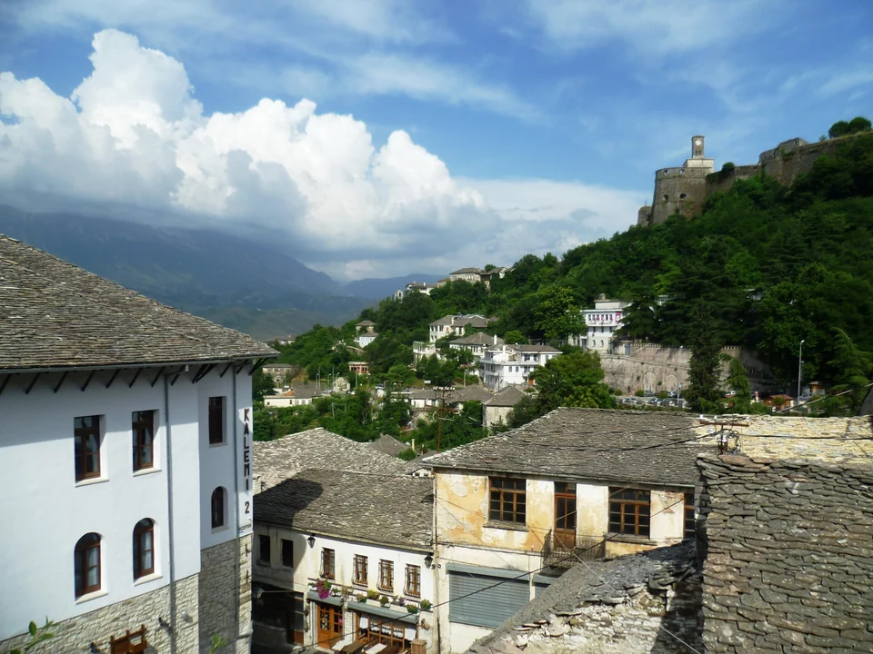 Slate-roofed stone houses of Gjirokastër's old town below the castle and its clock tower on a green hill