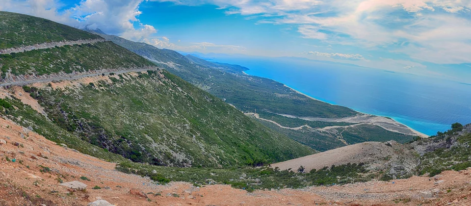 Panoramic view from the Llogara Pass of green mountainsides falling to the turquoise Ionian Sea on the Albanian Riviera