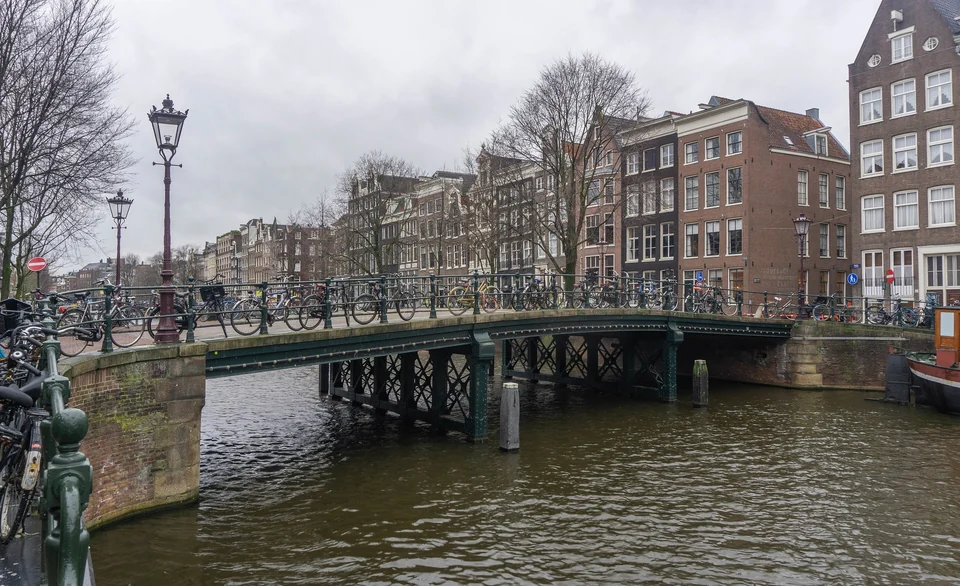Fahrräder parken auf einer Backsteinbrücke über einer ruhigen Gracht, gesäumt von hohen Häusern in Amsterdam