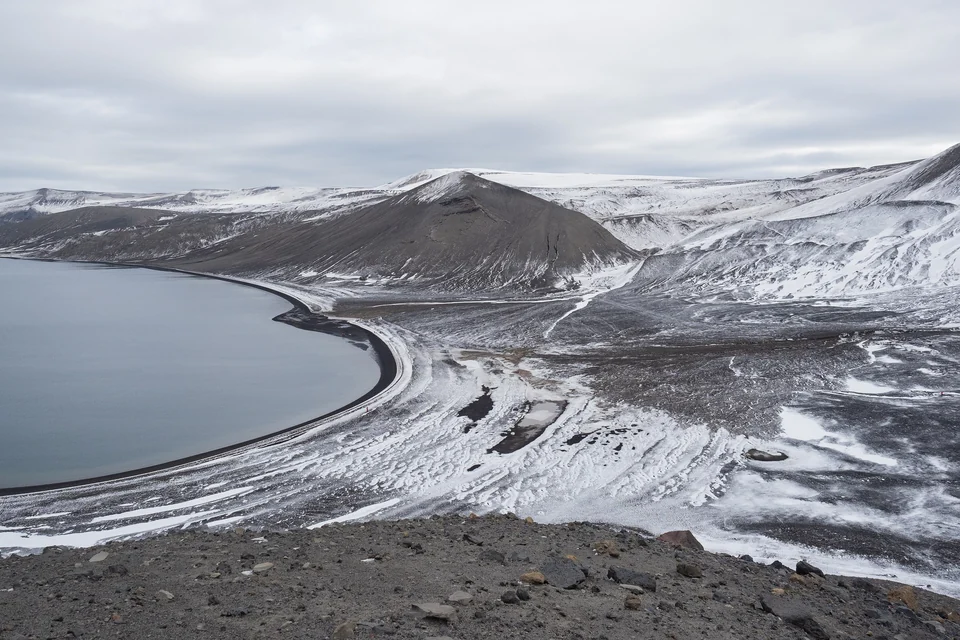 Curving black-sand beach of Pendulum Cove beside gray water, with snow-streaked volcanic slopes on Deception Island