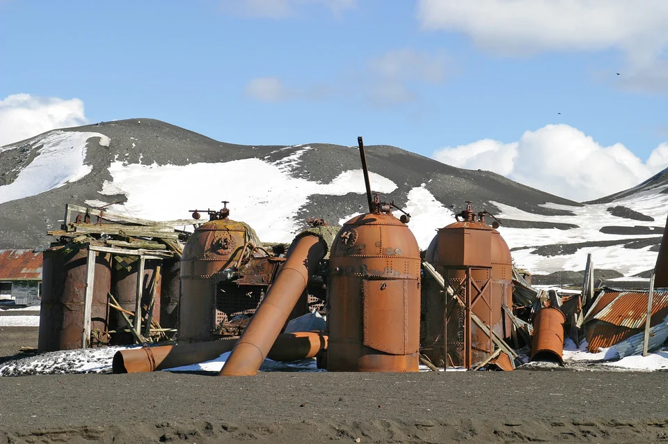 Rusting boilers of the old whaling station on the black volcanic beach of Whalers Bay, Deception Island, with snowy hills