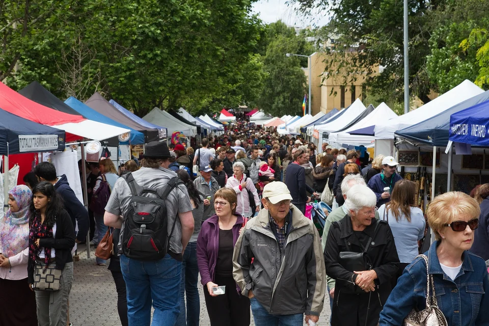 Crowds walking between white market stalls under trees at Salamanca Market in Hobart, Tasmania