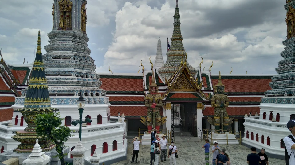Gekachelte Chedis und zwei riesige Wächterfiguren an einem Tor im Komplex des Großen Palastes in Bangkok