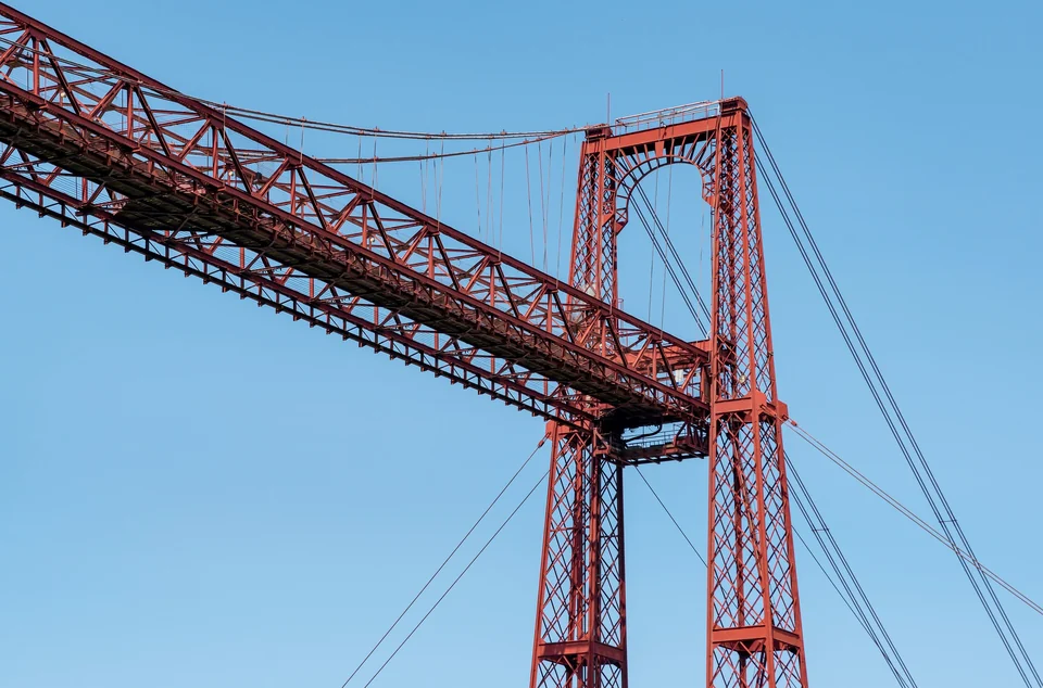 Red iron towers and upper walkway of the Vizcaya Bridge in Portugalete against a clear blue sky