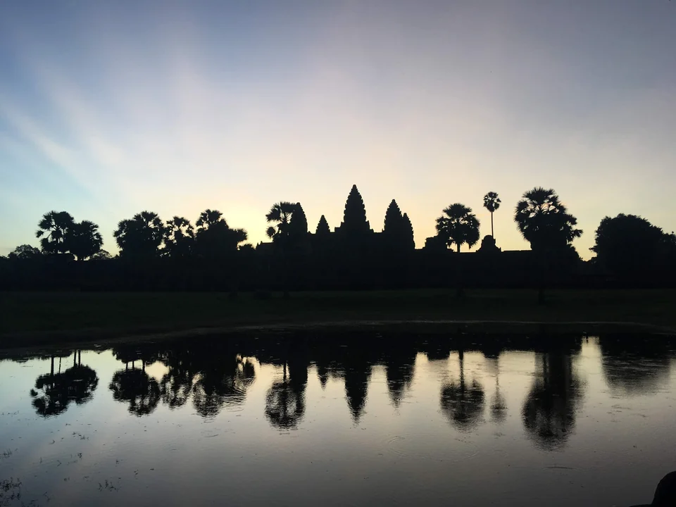 Angkor Wat's towers silhouetted against a pale dawn sky and reflected in the pond in front of the temple