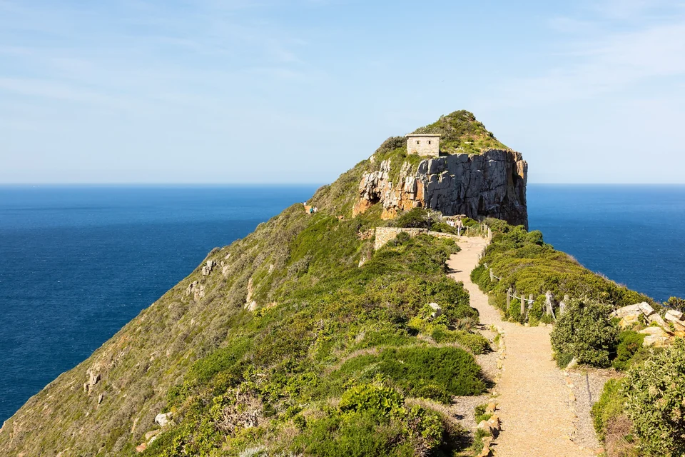 Footpath leading along a green ridge to the old lighthouse on the cliffs of Cape Point above the ocean