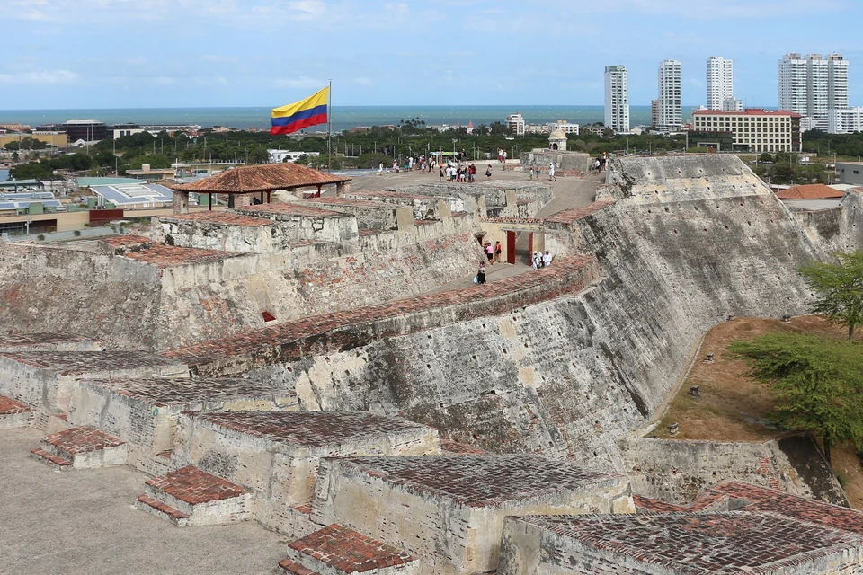Sloping stone ramparts of Castillo San Felipe de Barajas with the Colombian flag and Bocagrande towers behind