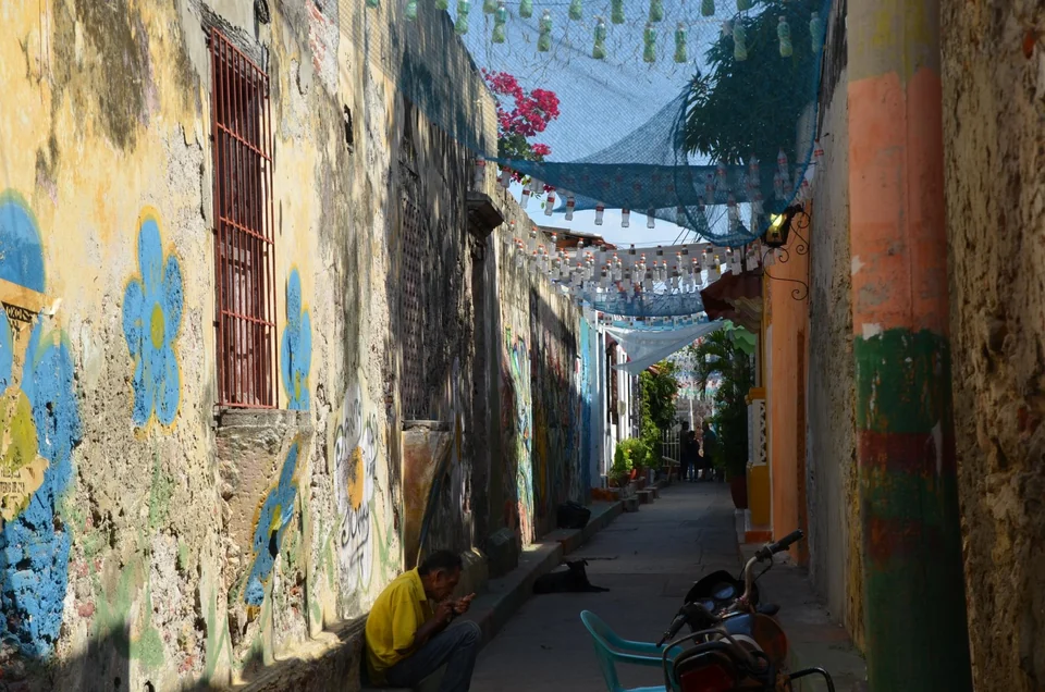 Narrow Getsemaní alley in Cartagena with painted murals on the walls and decorations strung overhead