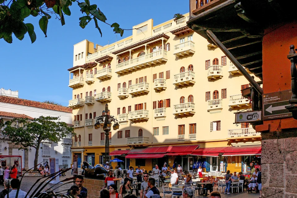 Café terraces and a tall yellow colonial building with balconies on Plaza de Santo Domingo in Cartagena