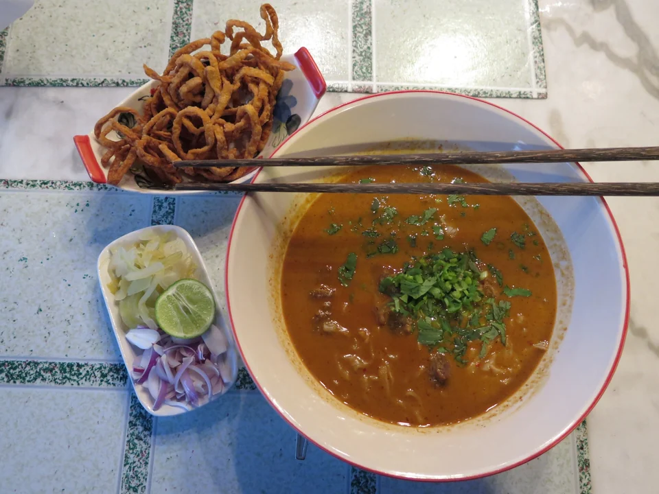 A bowl of khao soi curry noodle soup with crispy fried noodles on top, served in Chiang Mai