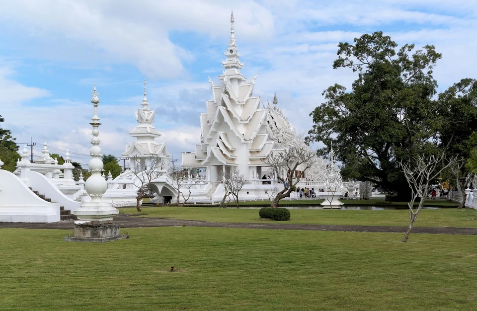 The white, mirror-studded ubosot of Wat Rong Khun, the White Temple in Chiang Rai, reflected in a pond