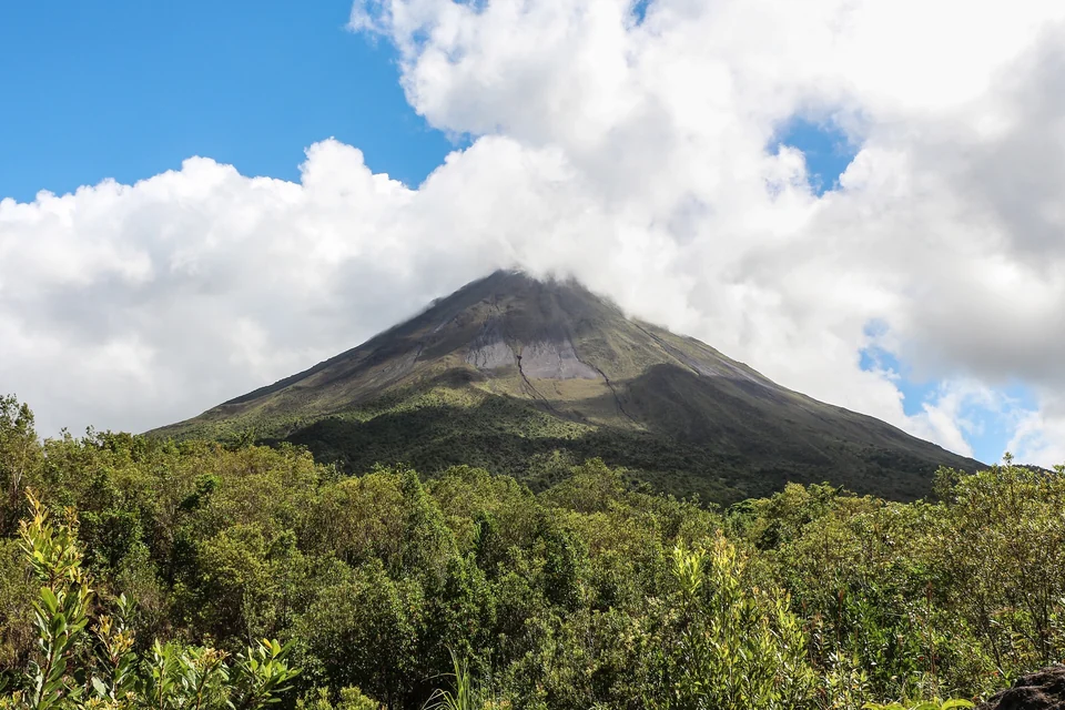 Cone of Arenal Volcano rising above green forest near La Fortuna, Costa Rica, with clouds around the summit