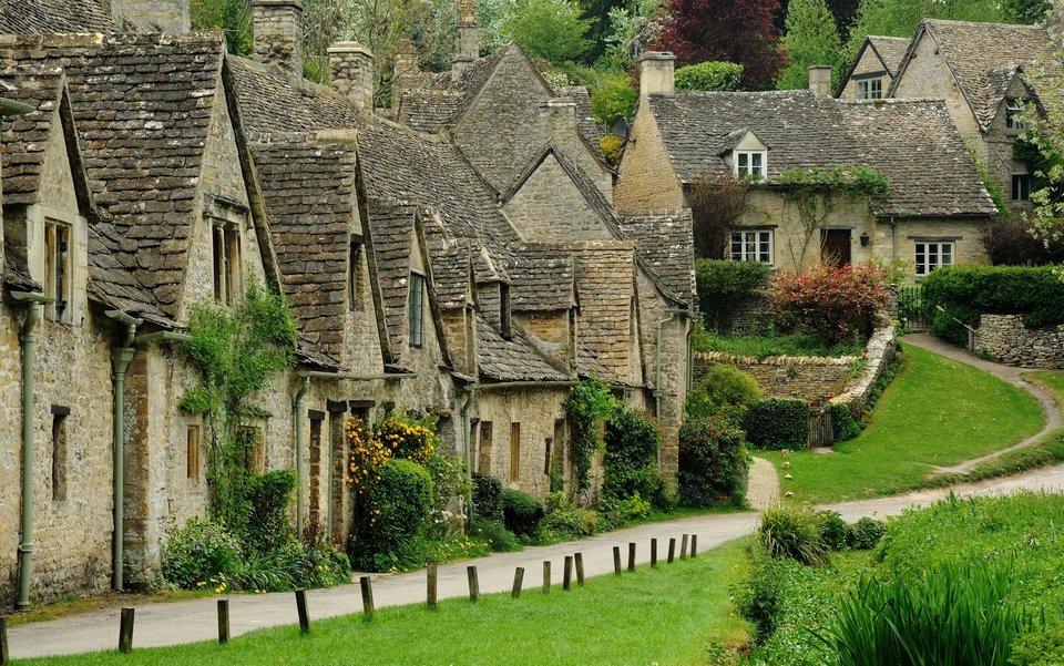 Arlington Row in Bibury, a line of steep-roofed stone weavers' cottages above a green meadow in the Cotswolds