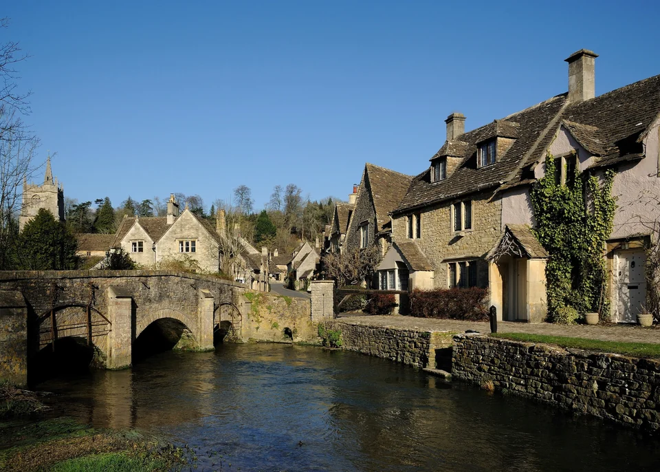 Stone bridge over the By Brook in Castle Combe with stone cottages and the church tower behind