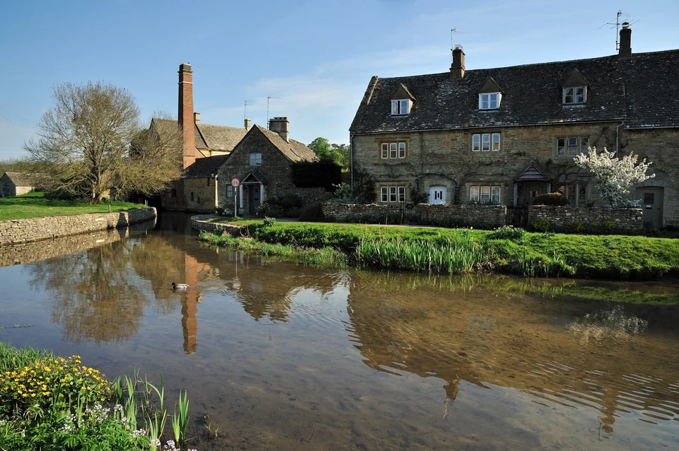 The old mill with a red brick chimney reflected in the River Eye at Lower Slaughter on a spring day