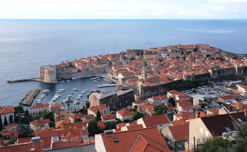 Dubrovnik's walled Old Town and Old Port seen from the hillside, with red roofs and the open Adriatic beyond