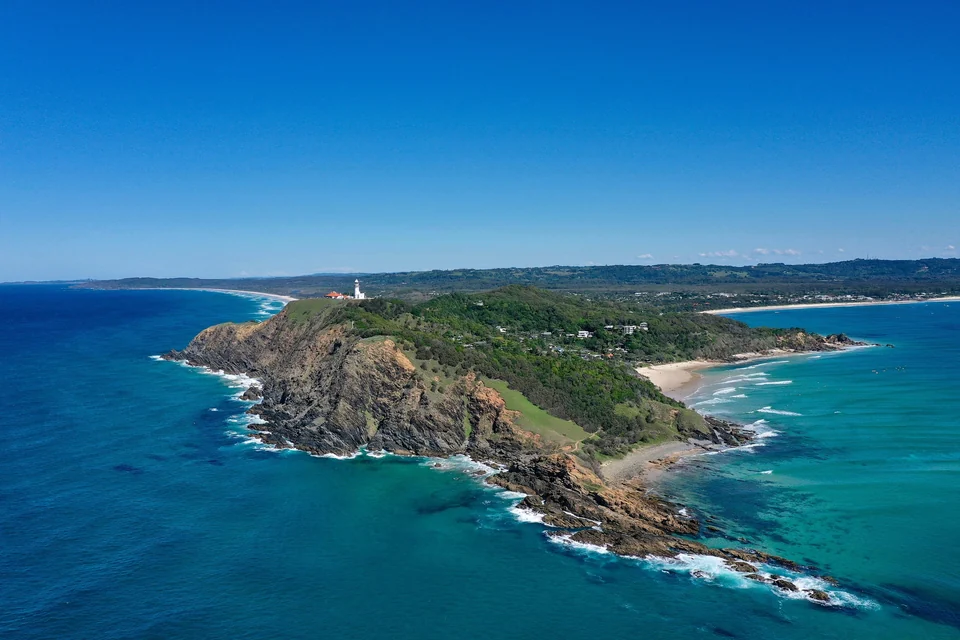 Aerial view of Cape Byron with its white lighthouse, surf beaches and green hinterland in Byron Bay, New South Wales