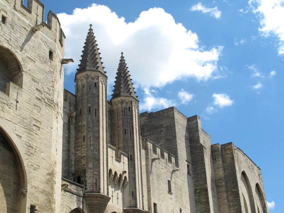 Gothic towers and high stone walls of the Palais des Papes in Avignon under a blue sky with white clouds