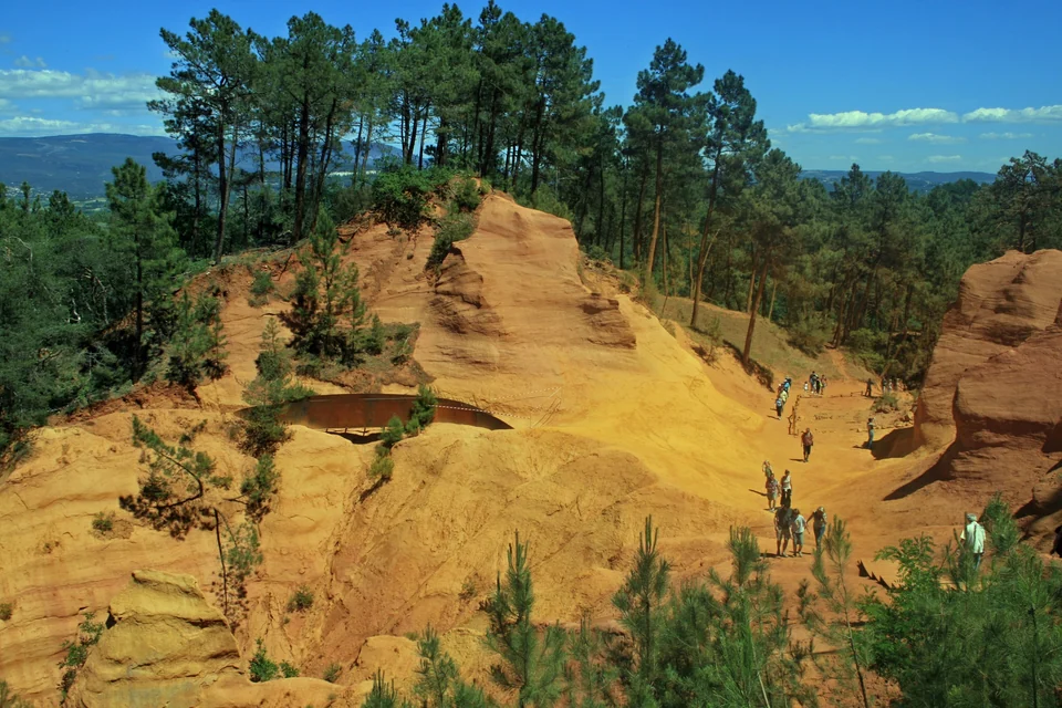 Orange and red ochre cliffs surrounded by green pine trees on the Sentier des Ocres in Roussillon, Provence