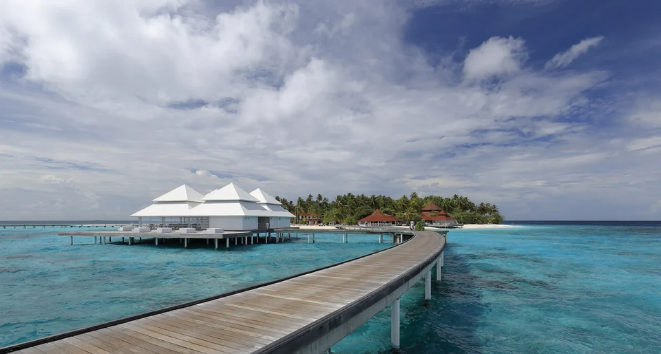 Wooden jetty leading to white-roofed overwater pavilions above a turquoise lagoon in Ari Atoll, Maldives