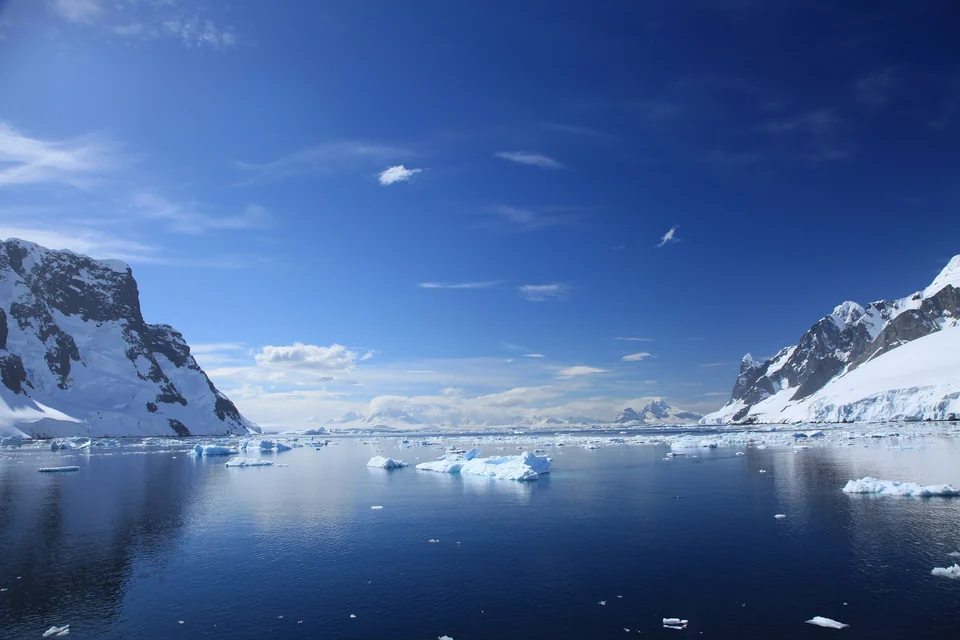 Calm blue water with floating ice between snow-covered mountains in the Lemaire Channel on the Antarctic Peninsula