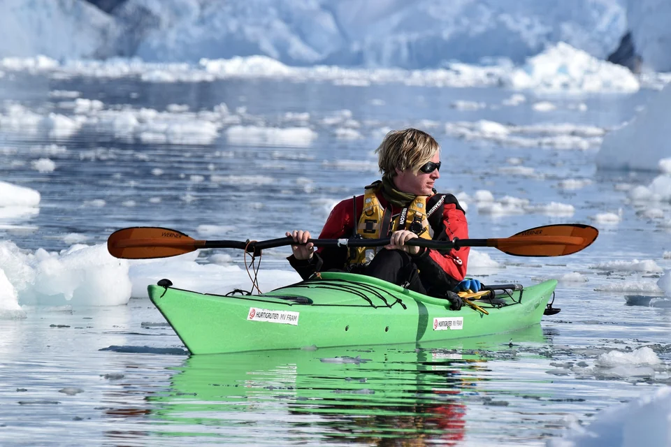 Sea kayaker paddling in calm water in front of a large glacier at Neko Harbour, Antarctic Peninsula