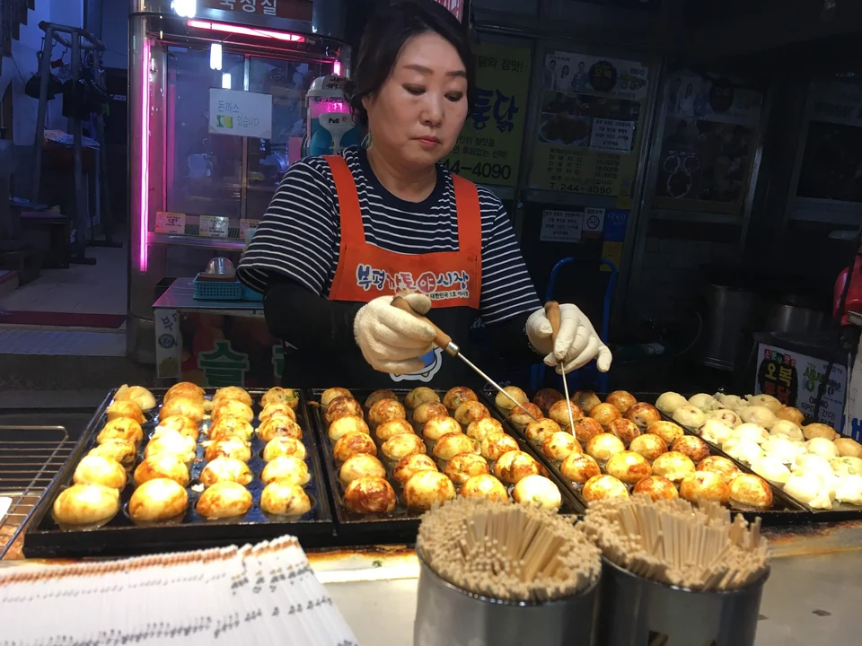 Vendor turning rows of round snacks on a hot plate at Bupyeong Kkangtong Night Market in Busan