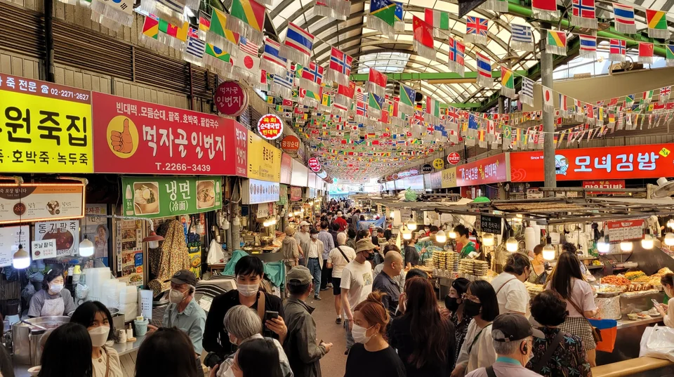 Crowds eating at food stalls under strings of flags inside Gwangjang Market in Seoul