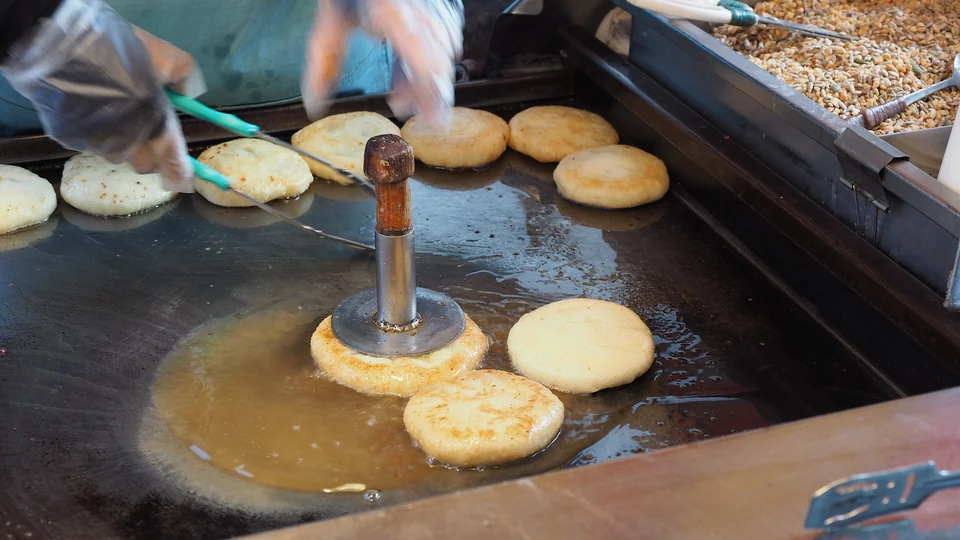Hotteok pancakes being pressed flat on an oiled griddle at a street stall in Busan, South Korea