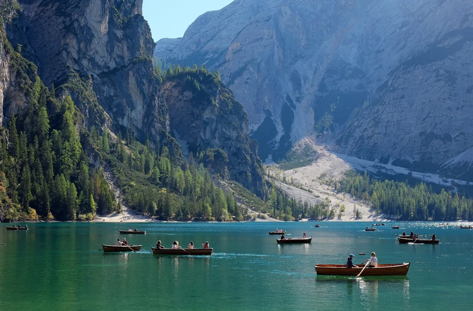 Wooden rowing boats moored on the green water of Lago di Braies with forested slopes behind in South Tyrol
