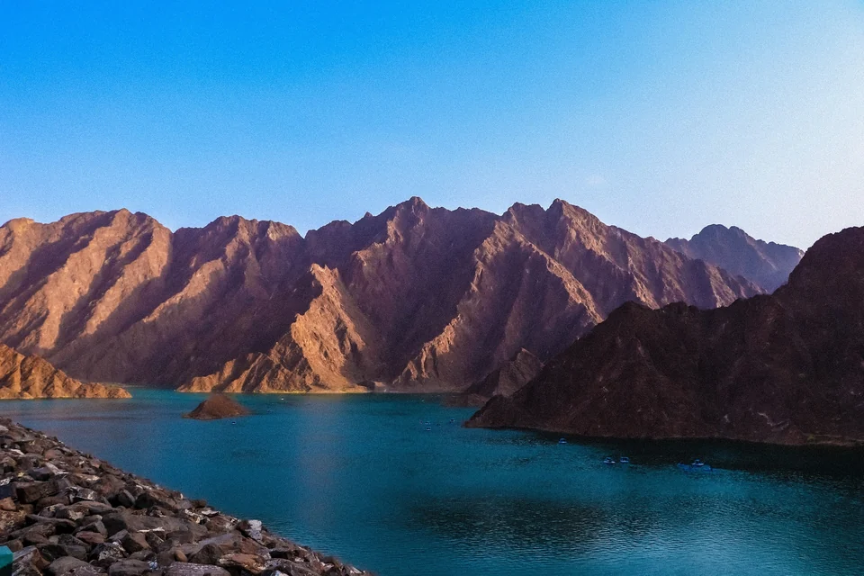 Turquoise reservoir at Hatta Dam surrounded by rugged Hajar Mountains with small boats on the water