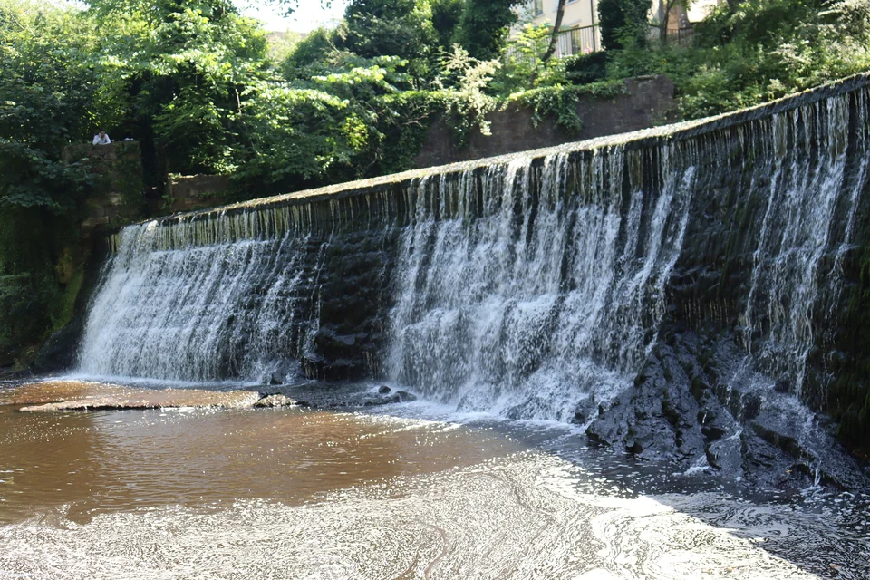 Weir on the Water of Leith beside restored stone buildings in Dean Village, Edinburgh