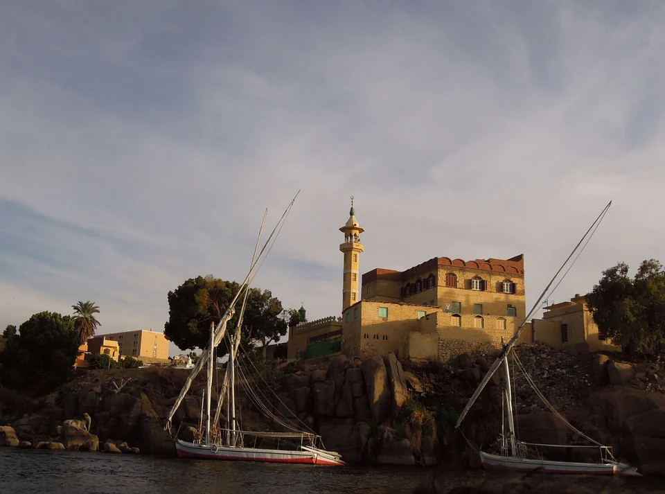 Traditional feluccas sailing on the Nile at sunset in Aswan with a mosque on the bank