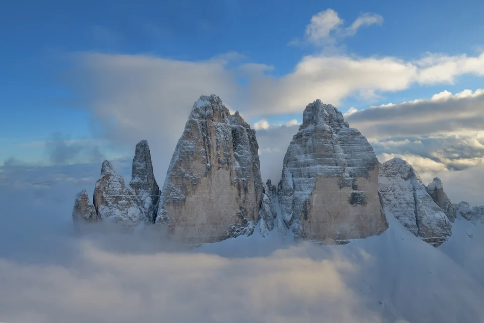 The three limestone peaks of the Tre Cime di Lavaredo in the Dolomites rising above clouds and snow