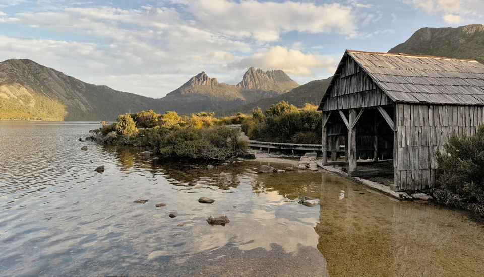 Wooden boat shed on the shore of Dove Lake with the jagged peaks of Cradle Mountain behind, Tasmania