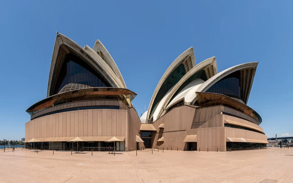 White sail-shaped roof shells of the Sydney Opera House under a clear blue sky, seen from the forecourt