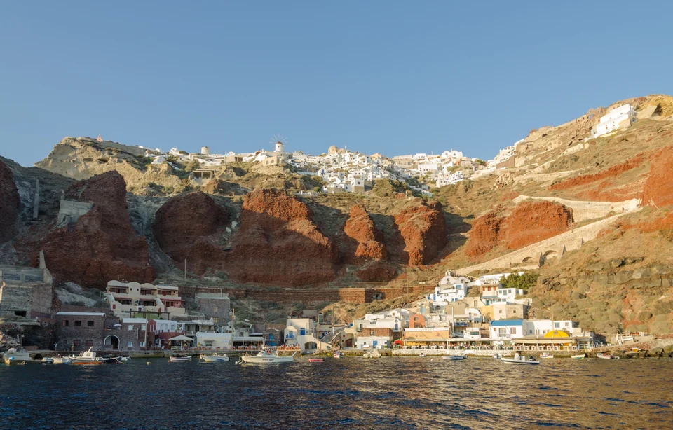 White houses and blue domes of Oia on the cliffs above the Santorini caldera, seen from a boat