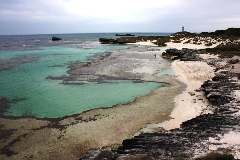 Turquoise lagoon and limestone reef at The Basin on Rottnest Island, with a lighthouse on the horizon