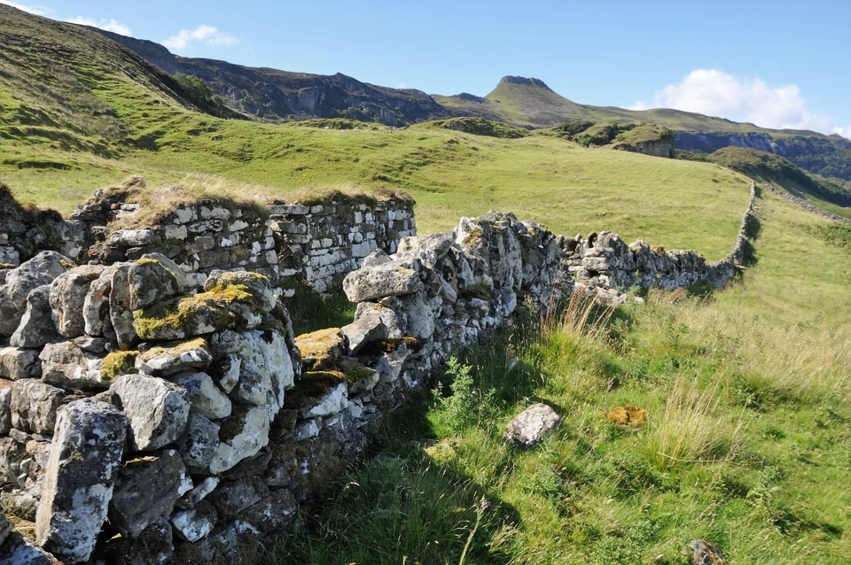 Lichen-covered stone walls of the abandoned township of Hallaig on Raasay below the flat-topped hill Dùn Caan