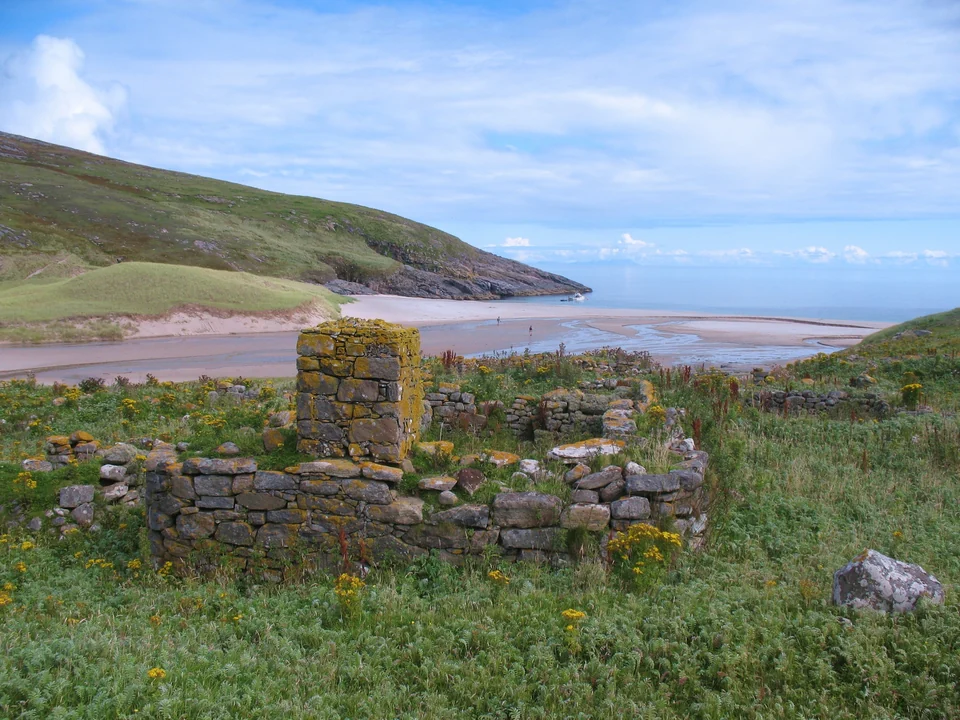 Roofless stone house ruins of the abandoned village on Mingulay in the Outer Hebrides, with grassy slopes behind