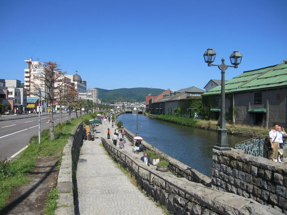 Old stone warehouses and lamps beside the Otaru Canal at dusk with a calm reflection on the water