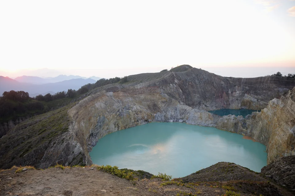 Pale turquoise Kelimutu crater lake at sunrise with a second lake behind the crater wall and hills of Flores beyond