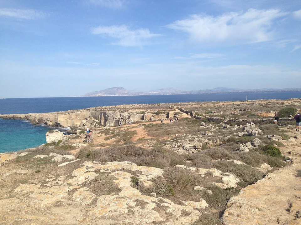Alte Steinbrüche und Radfahrer über der Cala Rossa auf Favignana, mit Trapani und dem Monte Erice jenseits des Meeres