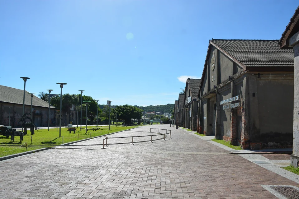 Brick-paved walkway beside gray gabled warehouses and the Hamasen railway museum at Pier-2 Art Center, Kaohsiung
