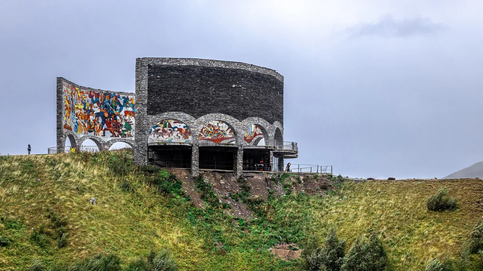 The curved stone Russia-Georgia Friendship Monument with colorful panels on a hillside near Gudauri