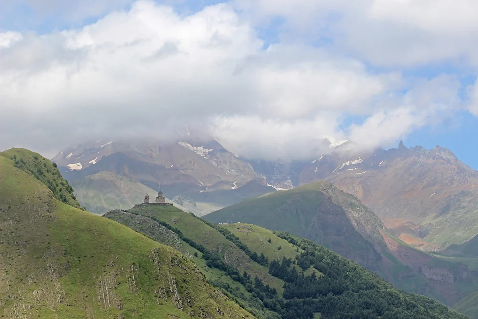 Gergeti Trinity Church on a ridge above Stepantsminda with the Kazbek massif and clouds behind it