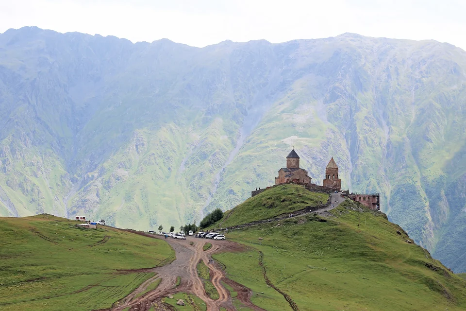 Gergeti Trinity Church on a green ridge above Stepantsminda with the Caucasus mountains rising behind it